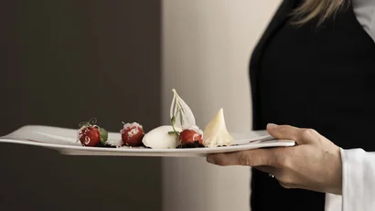 Cameriera che serve un piatto gourmet artisticamente impiattato su un piatto bianco